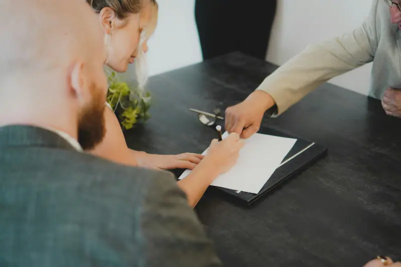 Pareja firmando un documento en una notaría con la asesoría de un abogado